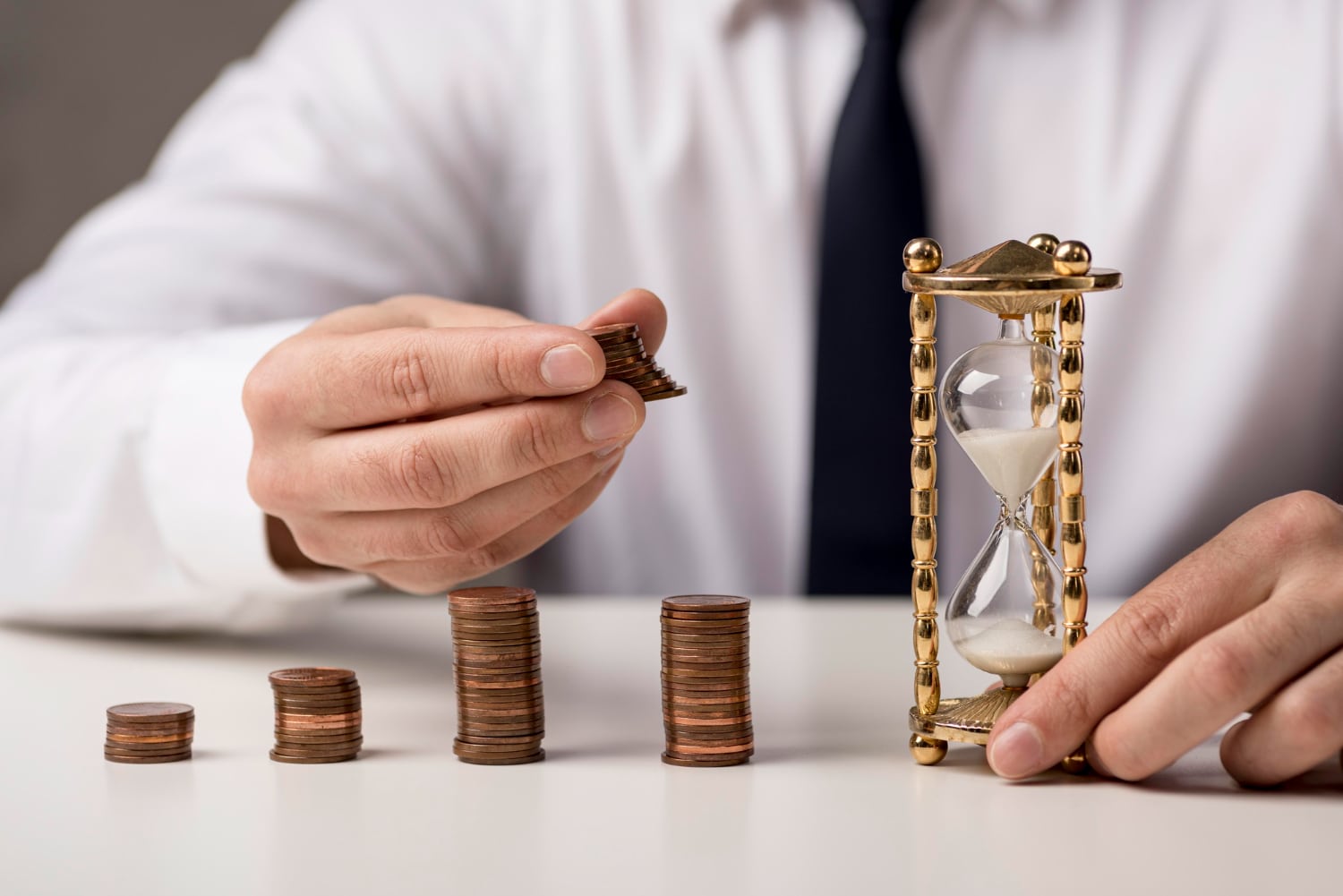 A businessman stacking coins beside an hourglass, symbolising time and investment management.