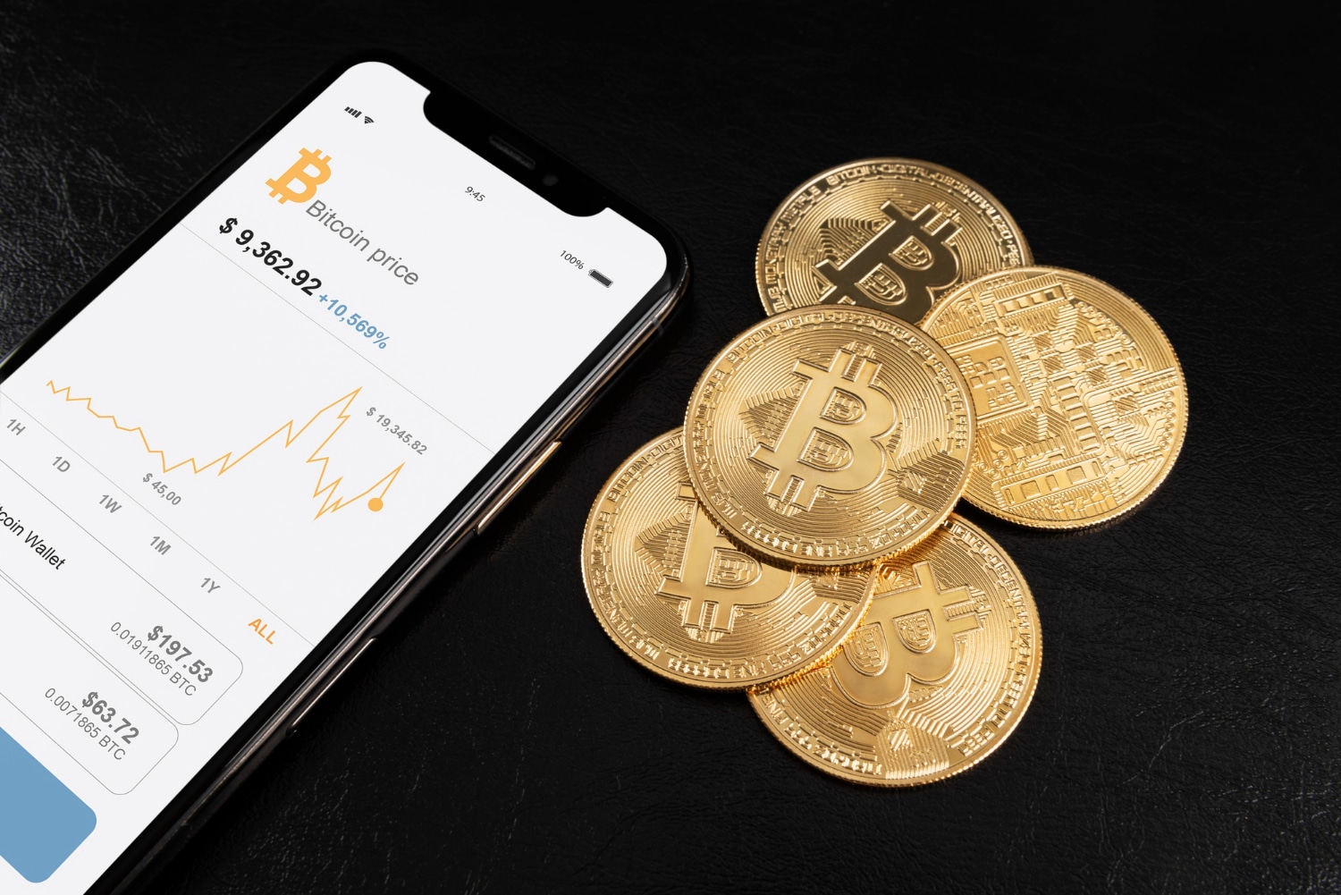 Smartphone displaying Bitcoin price on screen, surrounded by physical Bitcoin tokens on a black surface.