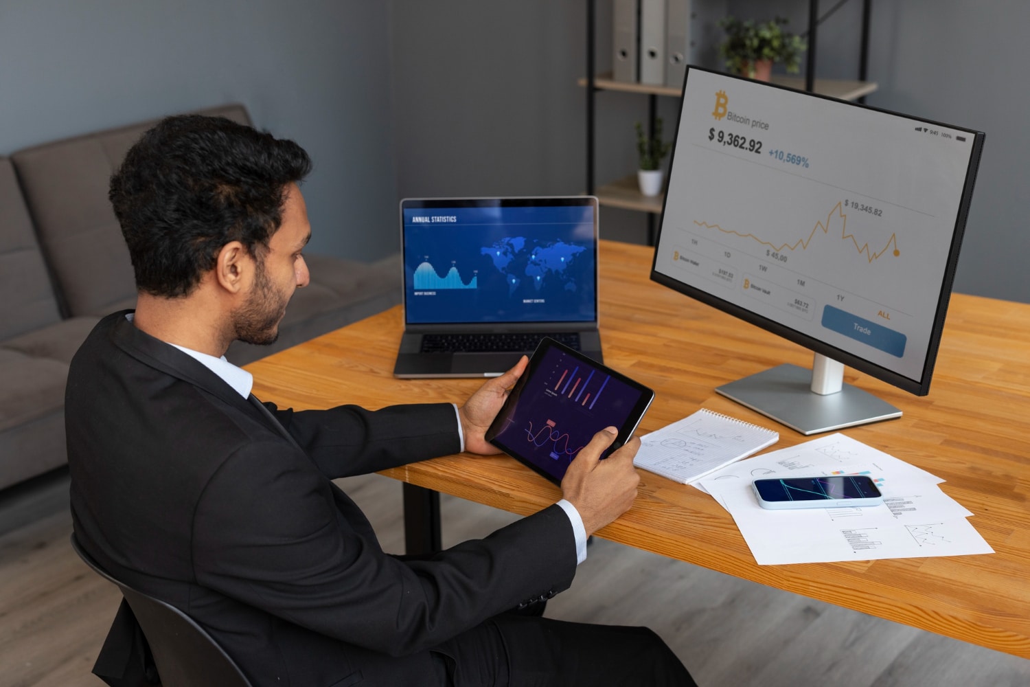 Businessman analyzing financial data on tablet with multiple screens showing graphs and statistics around him.
