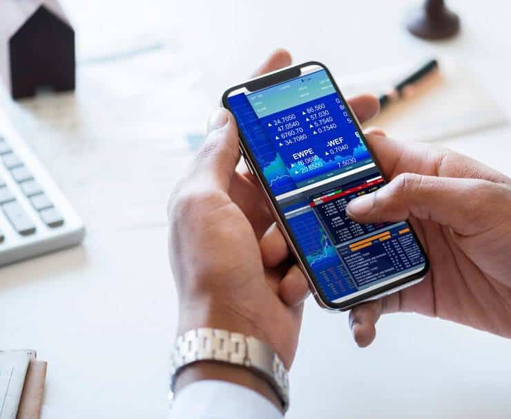 Person checking stock market data on a smartphone at an office desk.
