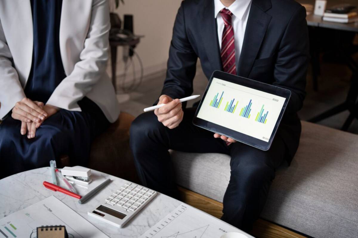 Two business professionals discussing data charts on a tablet in a modern office setting.