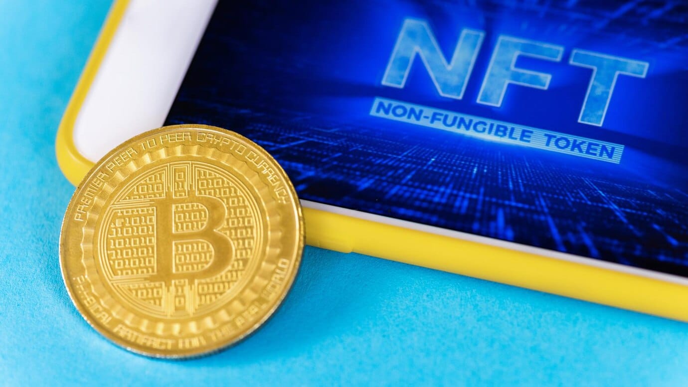 Bitcoin coin and a smartphone displaying NFT - Non-Fungible Token on a blue background.