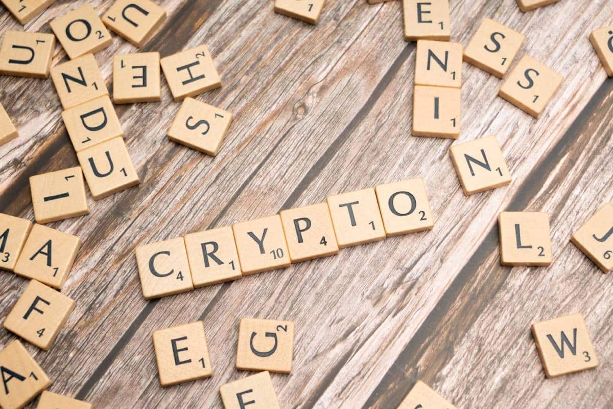 Scrabble tiles on a wooden surface spelling "CRYPTO" with scattered letters around.