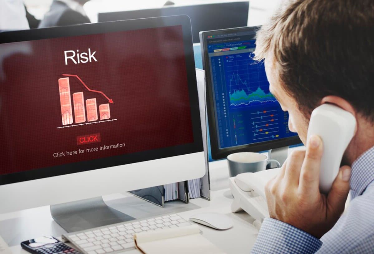 Man analyzing financial risk on a computer screen while talking on the phone in an office setting.